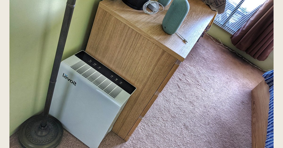 A top-down view of a room with a Levoit air purifier beside a desk and furniture.