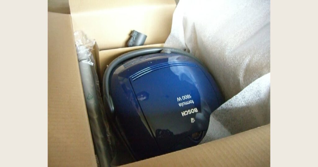 A blue canister vacuum packed in a cardboard box; its 1800 W label is visible